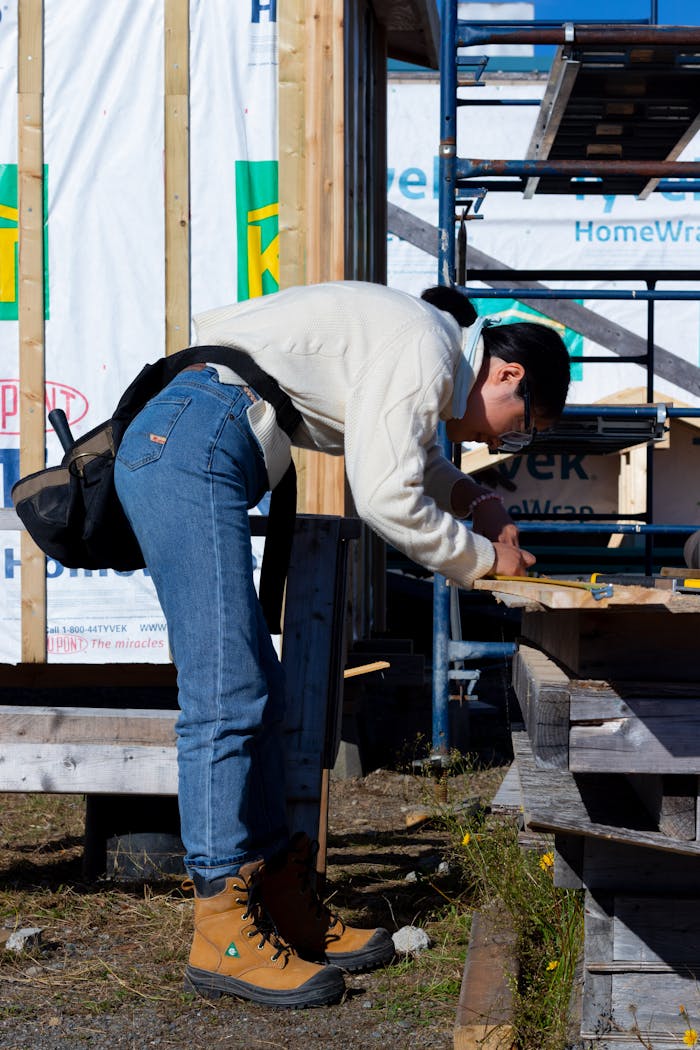 A person engaged in woodworking at a construction site, wearing boots and jeans.